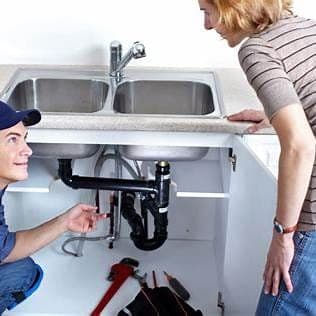 Plumber reviewing visible under-sink drain piping with a homeowner