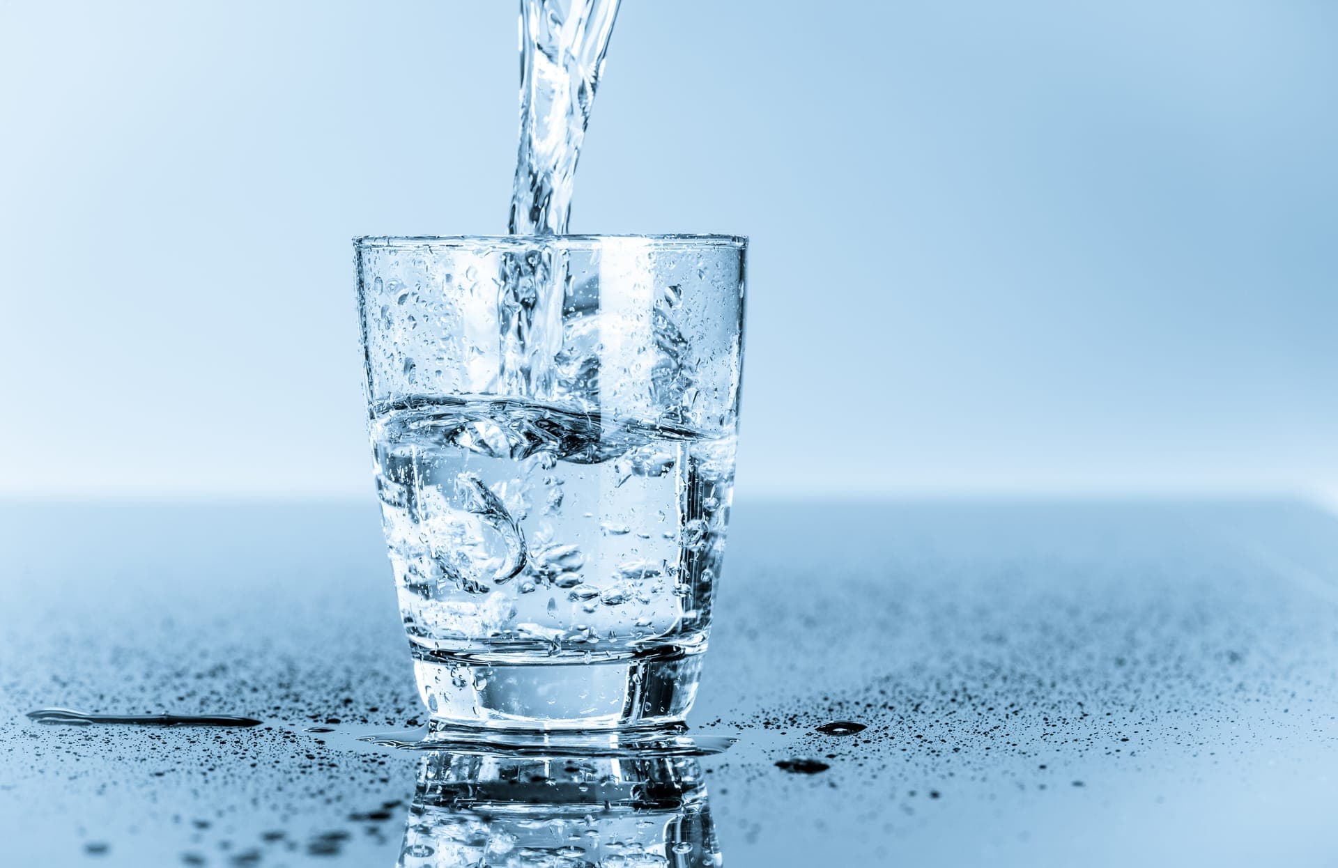 Water pouring into a clear drinking glass on a wet blue surface