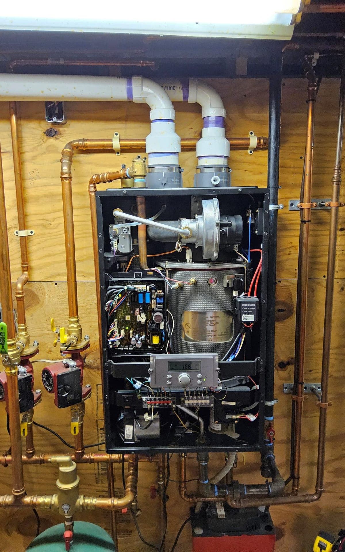 Open wall-mounted boiler cabinet with hydronic pumps and copper piping