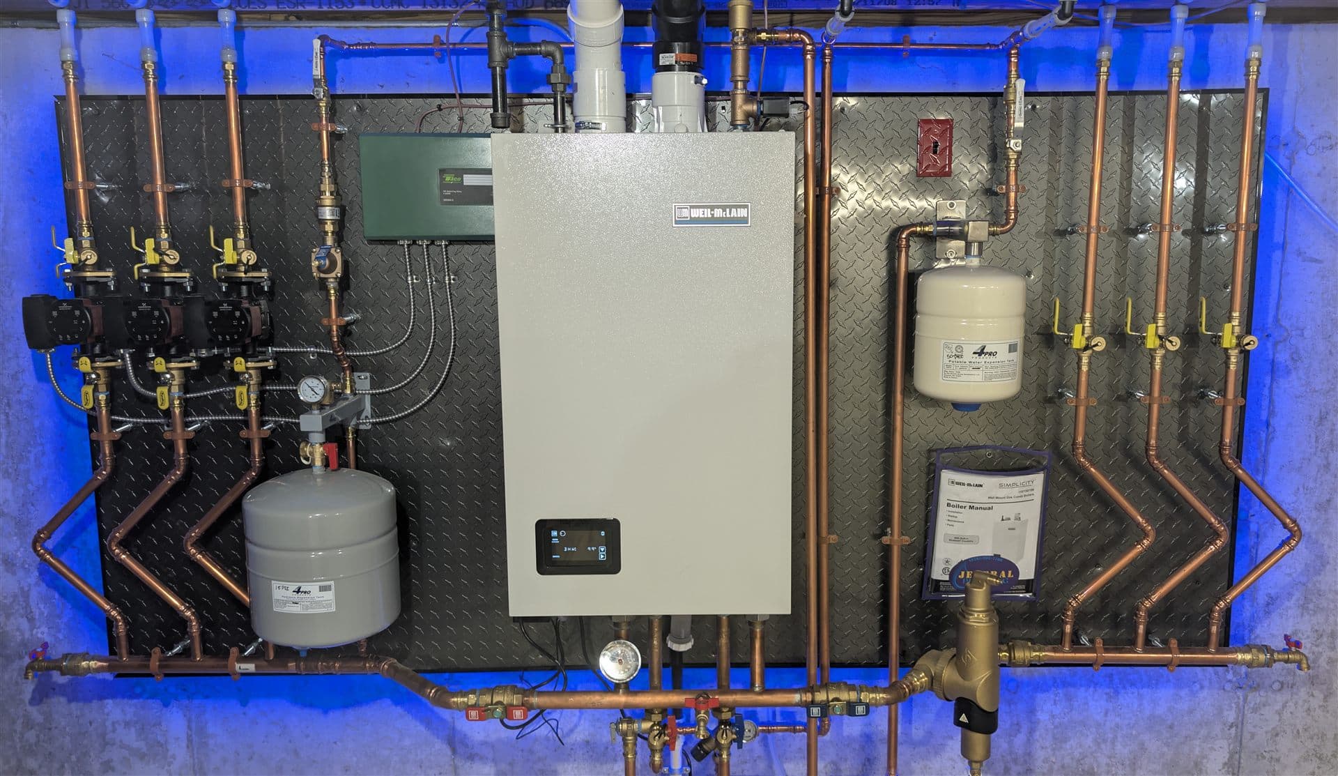 Weil-McLain Simplicity combi boiler installed by Jeneral Plumbing with copper zone manifolds and circulators on a backlit mounting board