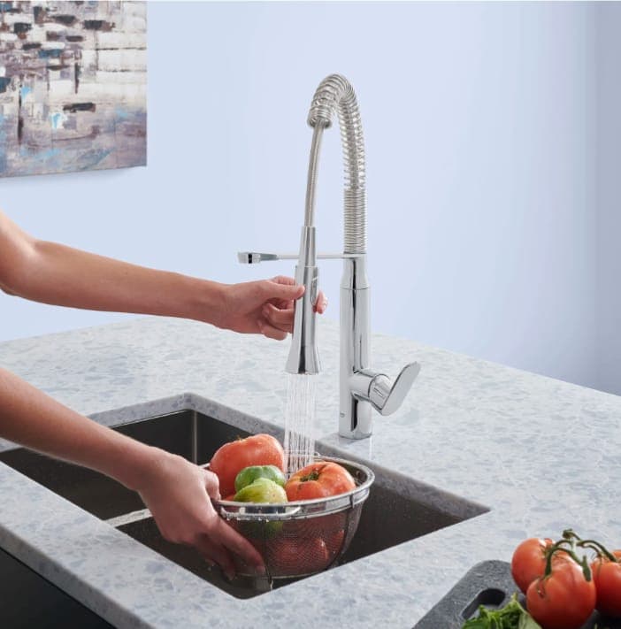 Person rinsing produce at a modern kitchen sink with a pull-down faucet