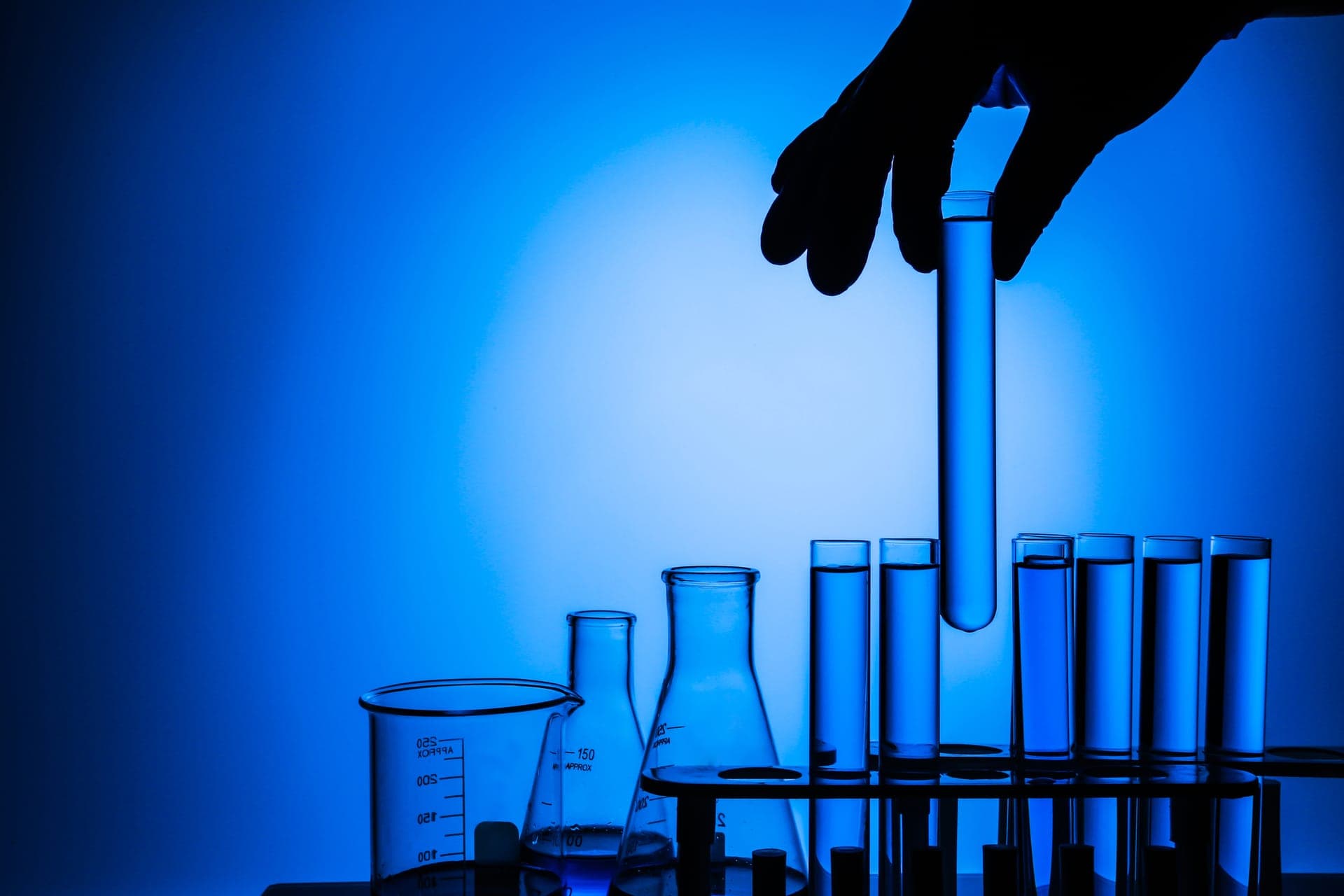 Gloved hand holding a water-filled test tube above laboratory glassware