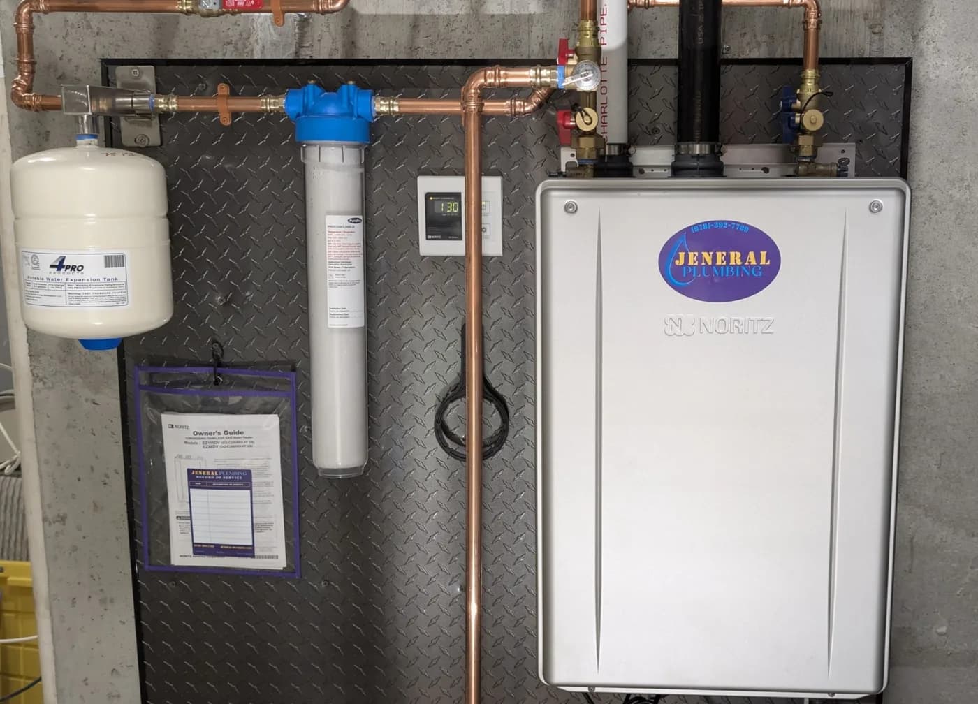 Noritz condensing tankless water heater with in-line filter and expansion tank, installed by Jeneral Plumbing on a custom diamond-plate wall panel