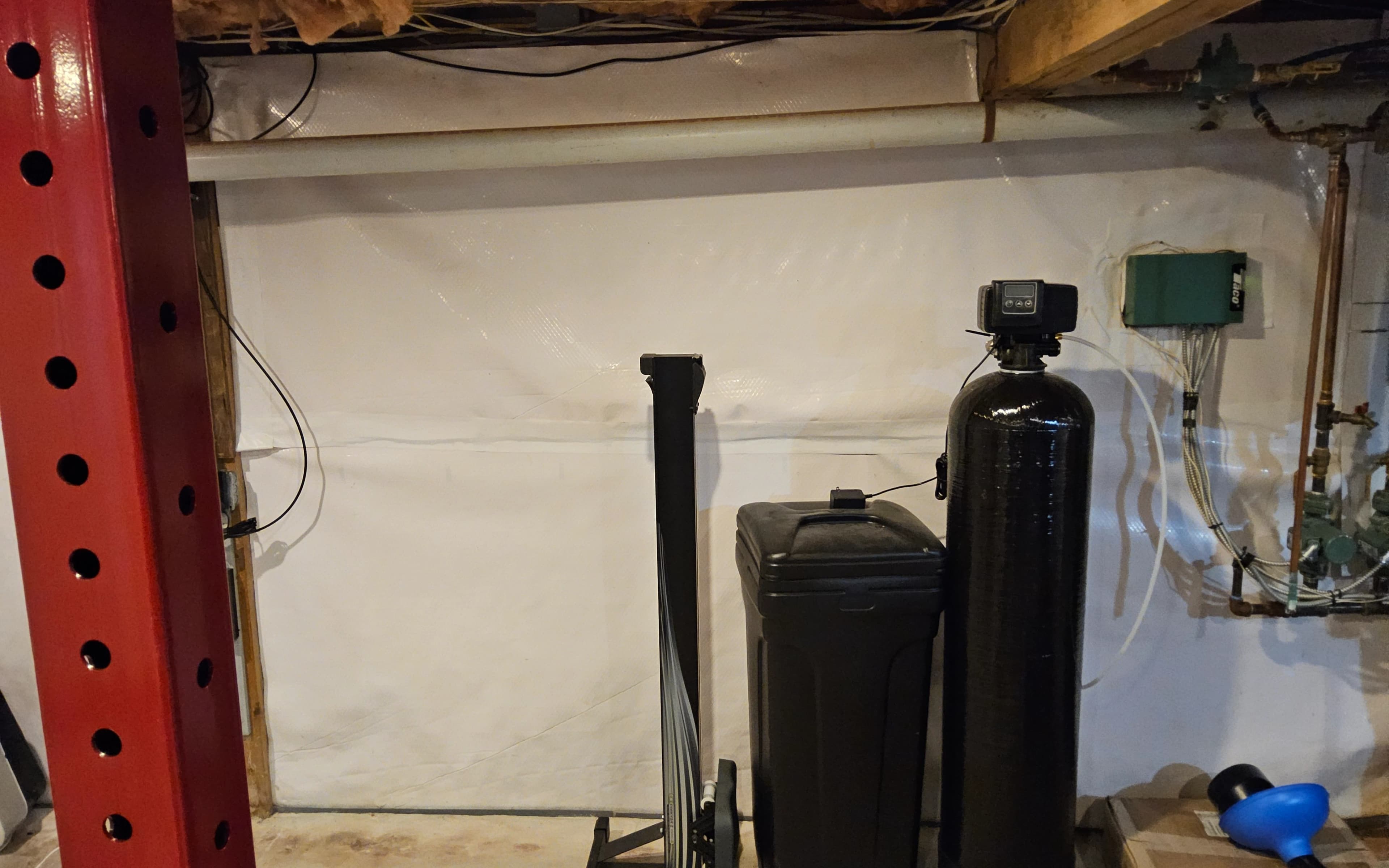 Tall black water-treatment tank and a shorter black tank against a basement wall with white sheeting.