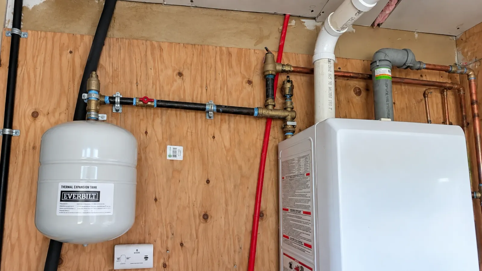 Gray thermal expansion tank and exposed piping beside a white wall-mounted heating appliance
