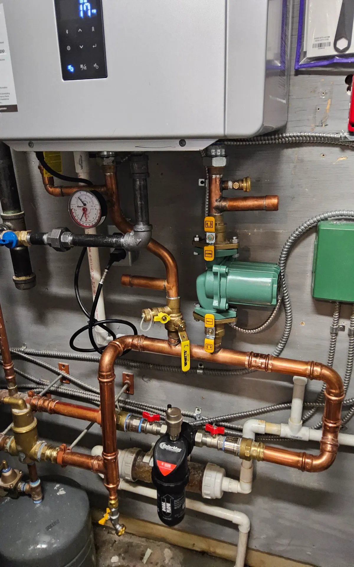Wall-hung boiler piping with a circulator pump, isolation valves, a pressure and temperature gauge, black-iron gas supply piping, and a magnetic dirt separator