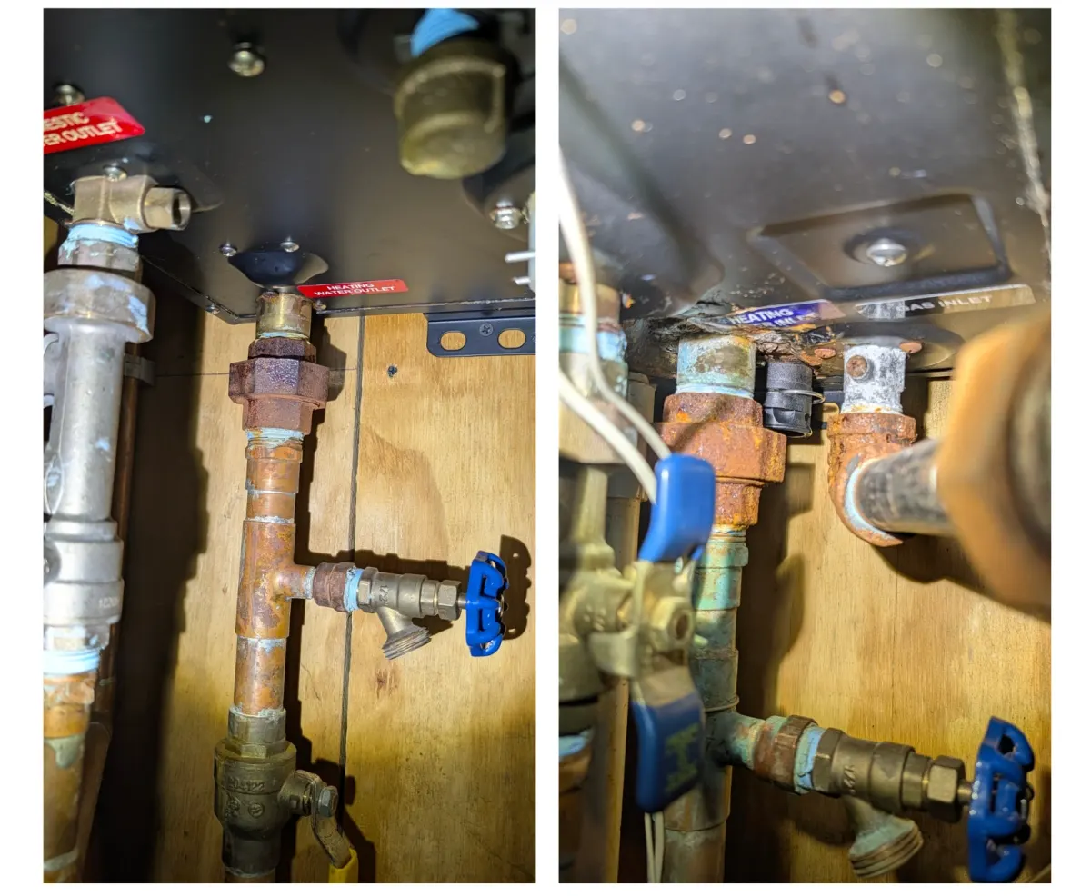 Underside of a combi boiler with rust and corrosion on the heating-water outlet union and the heating and gas inlet fittings, and a blue-handled drain valve